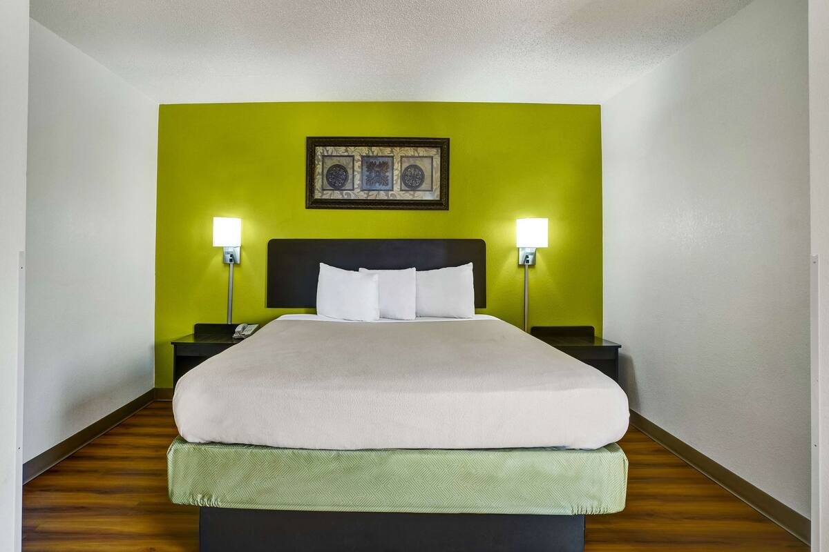 A hotel room with a bed, green walls, and two bedside lamps.