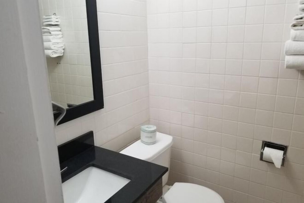 A bathroom with white tiles, a black sink, a toilet, and a mirror.