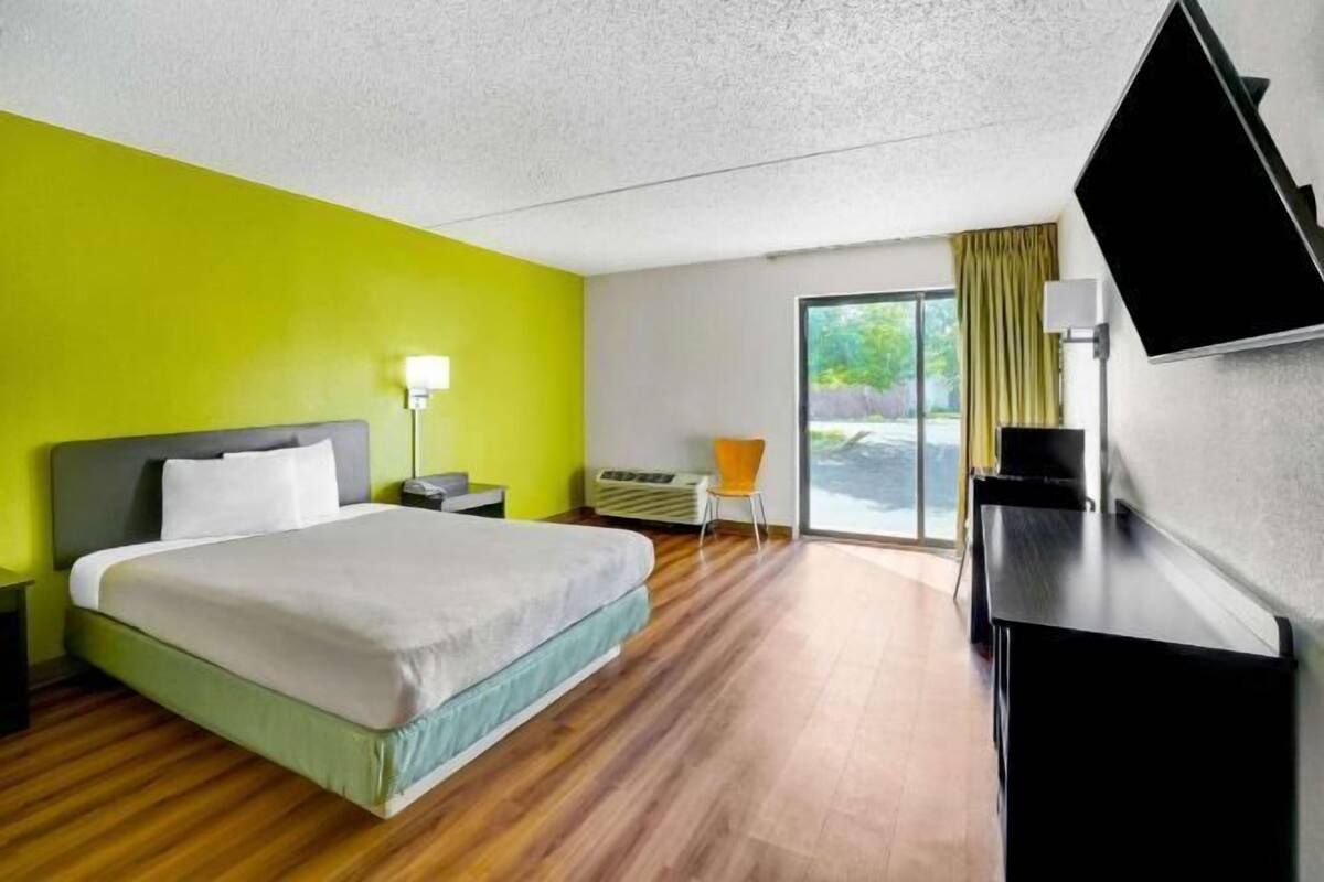 A hotel room with a bed, a desk, a chair, a TV, and a large window.