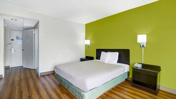 A hotel room with a bed, two bedside tables, a nightstand, a door, and a green wall.