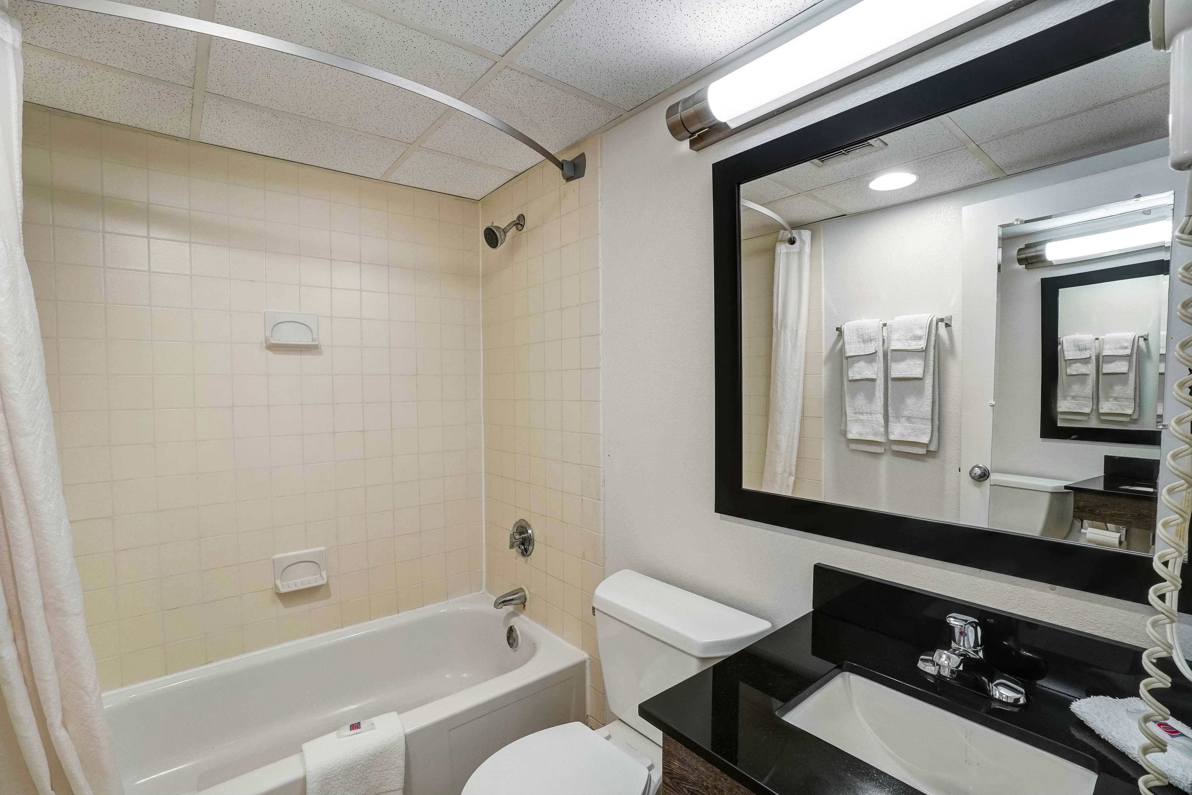 A bathroom with a bathtub, toilet, and sink, featuring a large mirror and tiled walls.