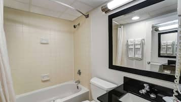 A bathroom with a bathtub, toilet, and sink, featuring a large mirror and tiled walls.