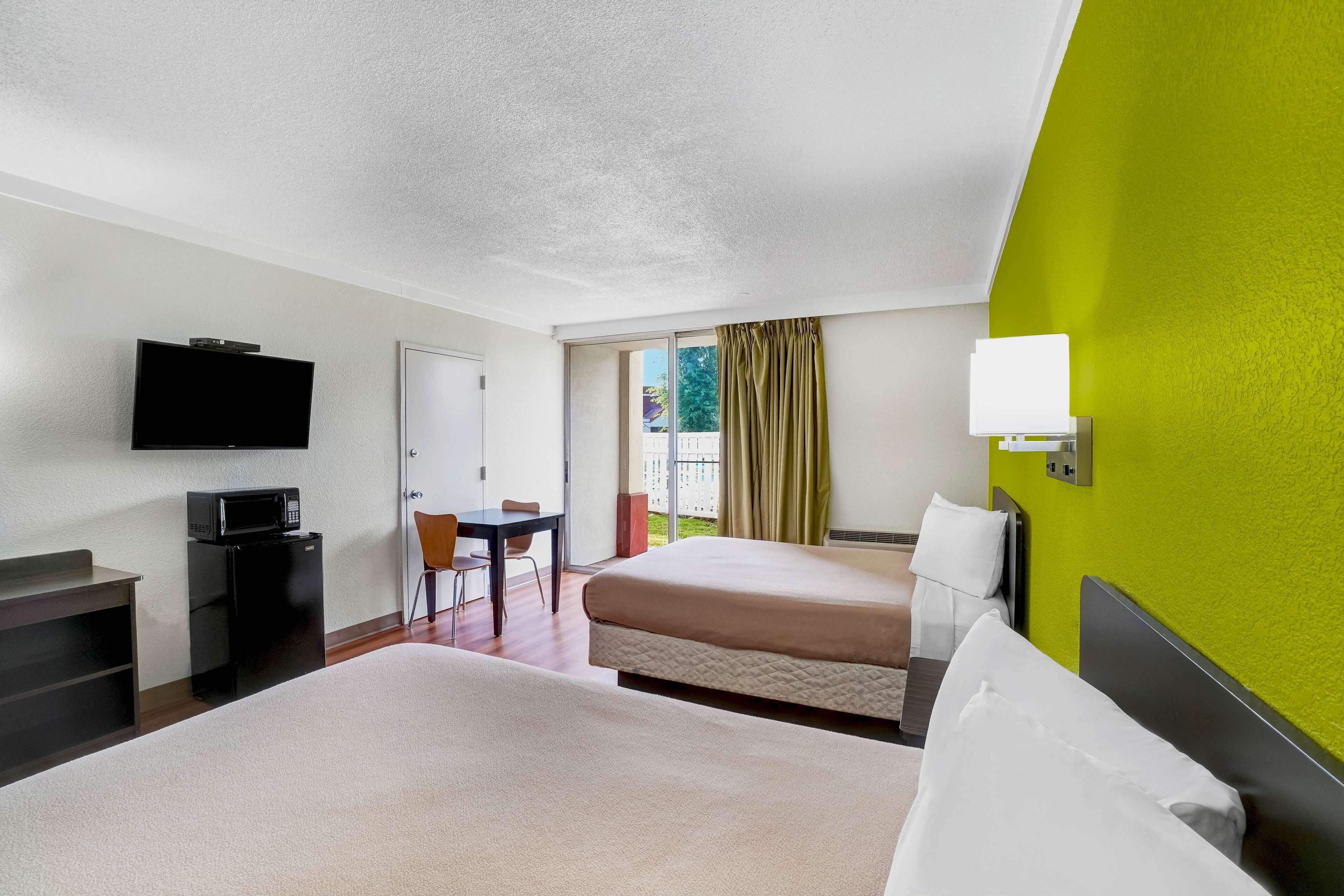 A hotel room with two beds, a desk with a computer, a TV, and a window with curtains.