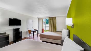 A hotel room with two beds, a desk with a computer, a TV, and a window with curtains.