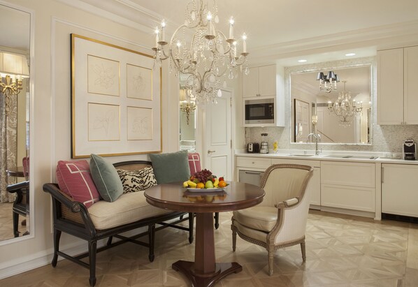 A dining area with a round table, two chairs, a chandelier, and a fruit bowl. - The Peninsula Beverly Hills (Beverly Hills)