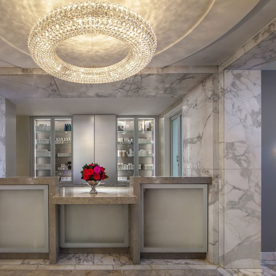 A lobby with marble walls, a central reception desk, and a chandelier.