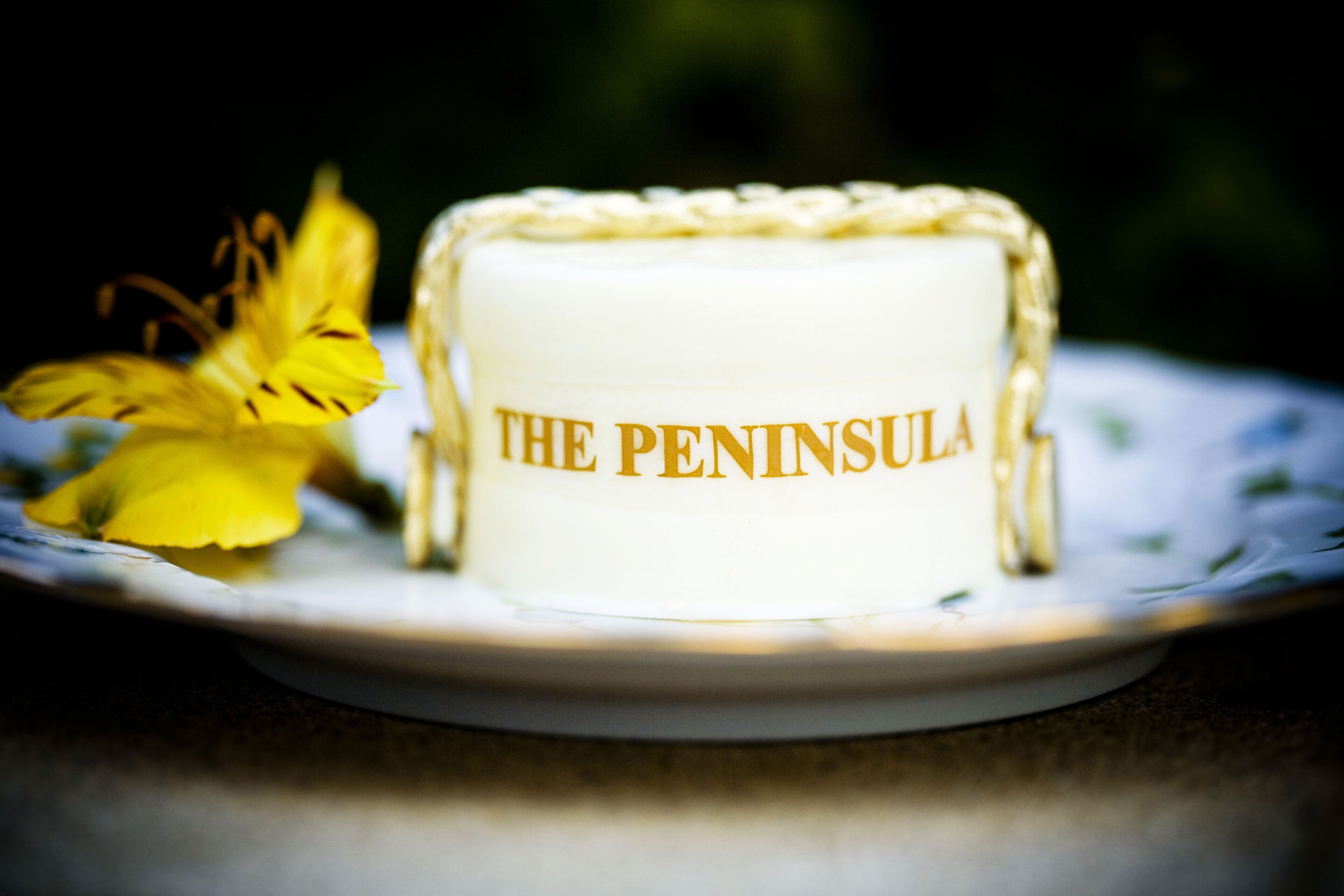 A cake with "THE PENINSULA" written on it, placed on a plate with a floral design.