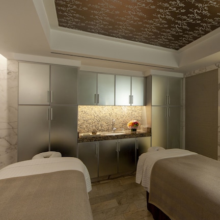 A modern hotel room with two beds, a bathroom with a large mirror, and a view of a textured wall.
