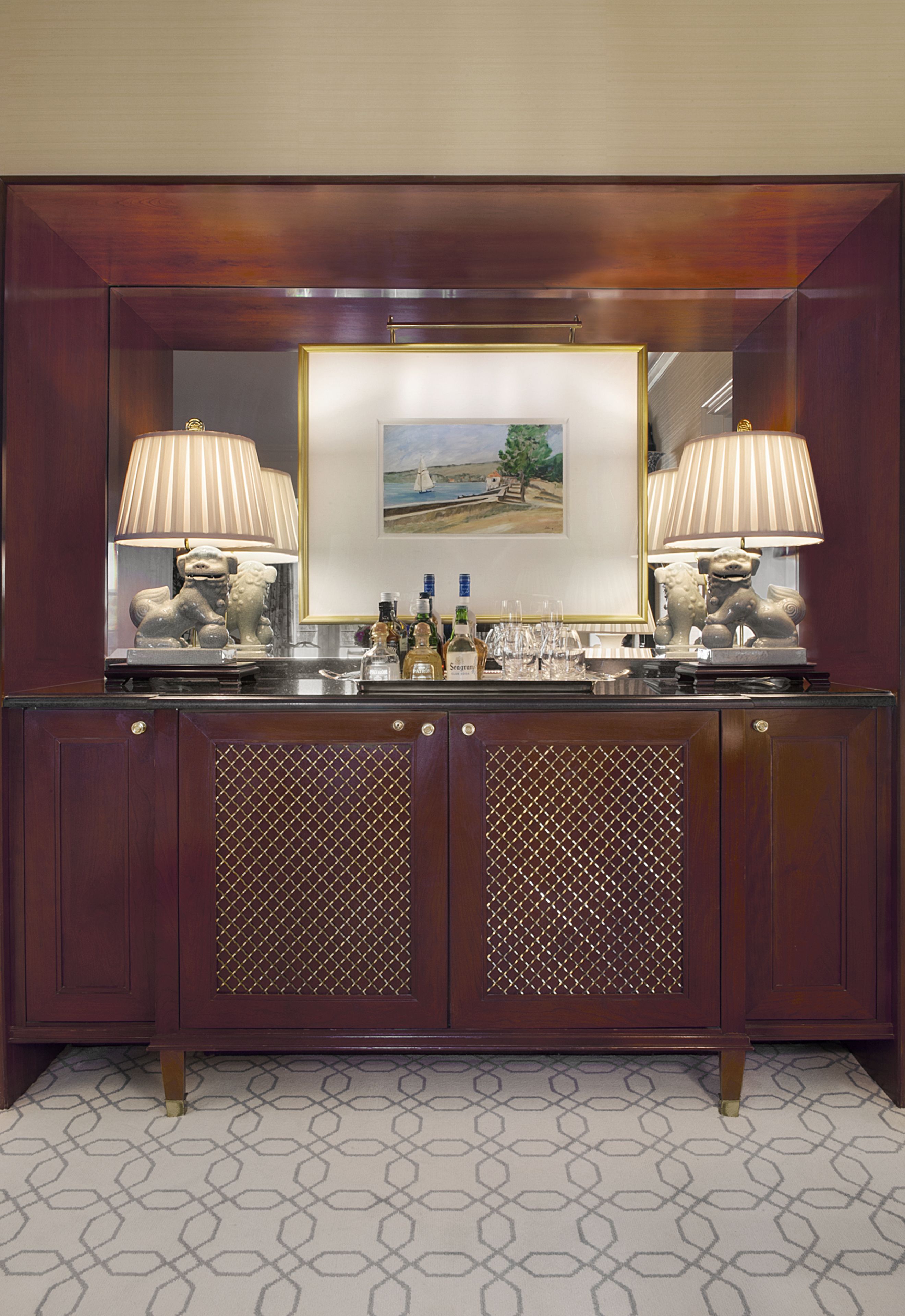 A dark wood console table with a mirrored surface, two lamps, and a framed landscape painting.