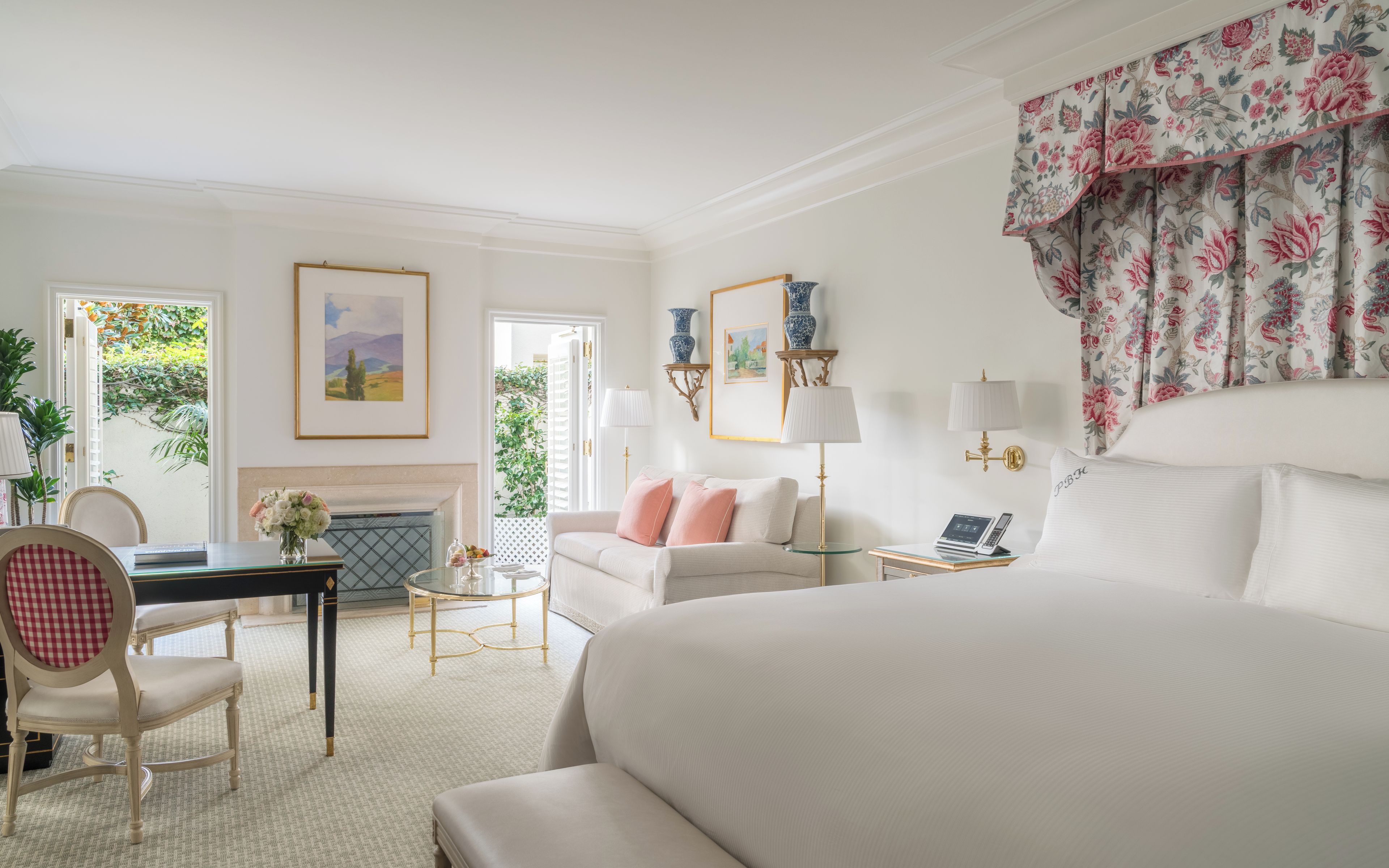 A hotel room with a large bed, a sitting area with a table and chairs, a fireplace, and a view of the outdoors.