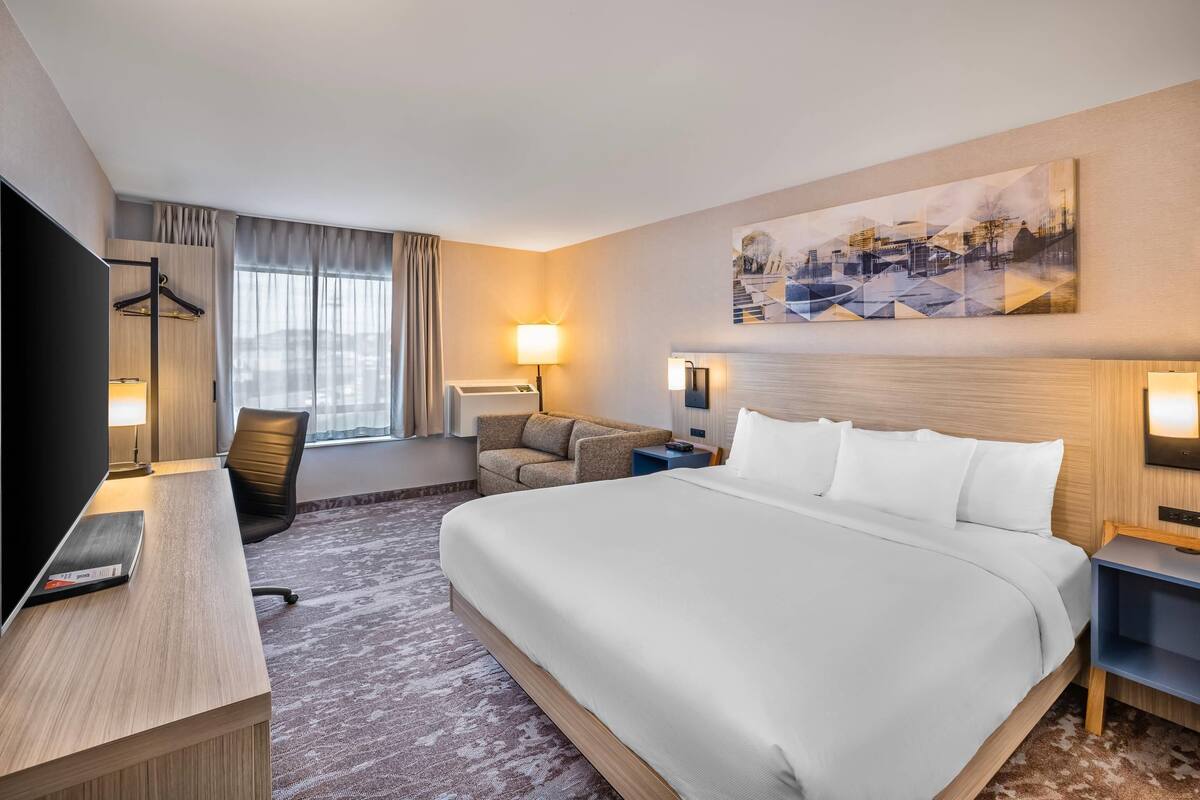 A hotel room with a large bed, a desk, a chair, a TV, and a painting on the wall.