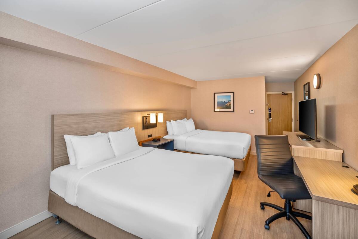 A hotel room with two beds, a desk, a chair, a TV, and a picture on the wall.