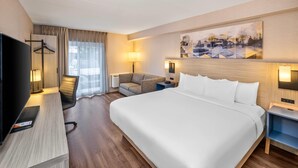 Ein Hotelzimmer mit einem großen Bett, einem Schreibtisch, einem Sessel, einem Fernseher und einem Bild an der Wand.