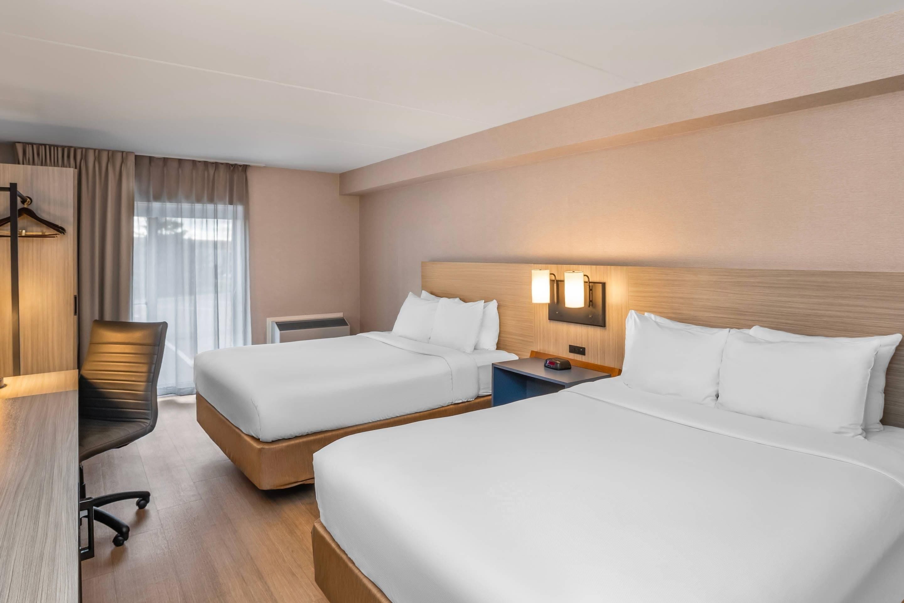 Ett hotellrum med två sängar, ett skrivbord, en stol och ett fönster med gardiner.