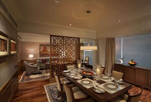 A dining area with a long table set for six, surrounded by chairs, with a decorative partition and a city view through the window.
