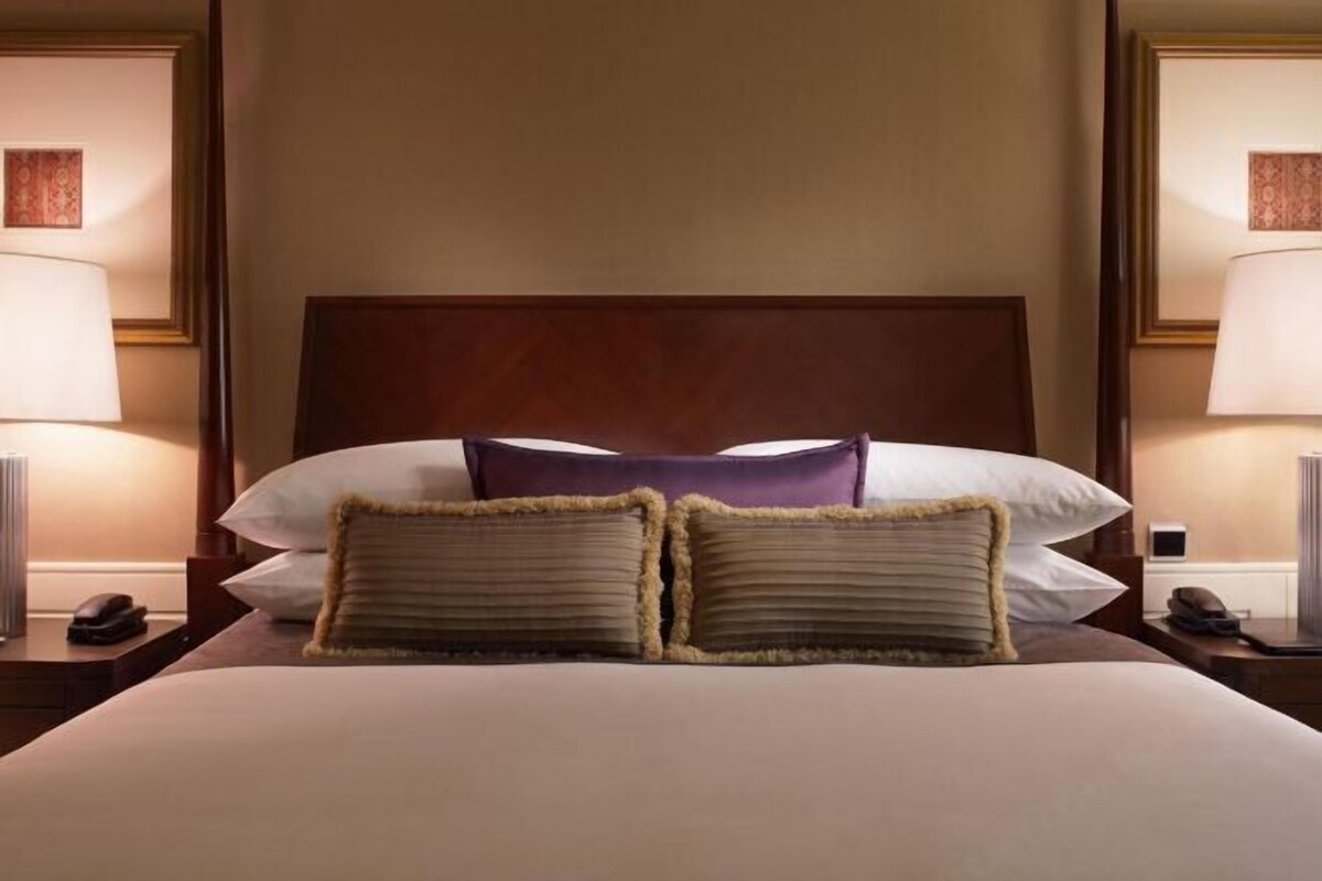 A hotel room with a large bed, two bedside lamps, a wooden headboard, and a framed picture on the wall.