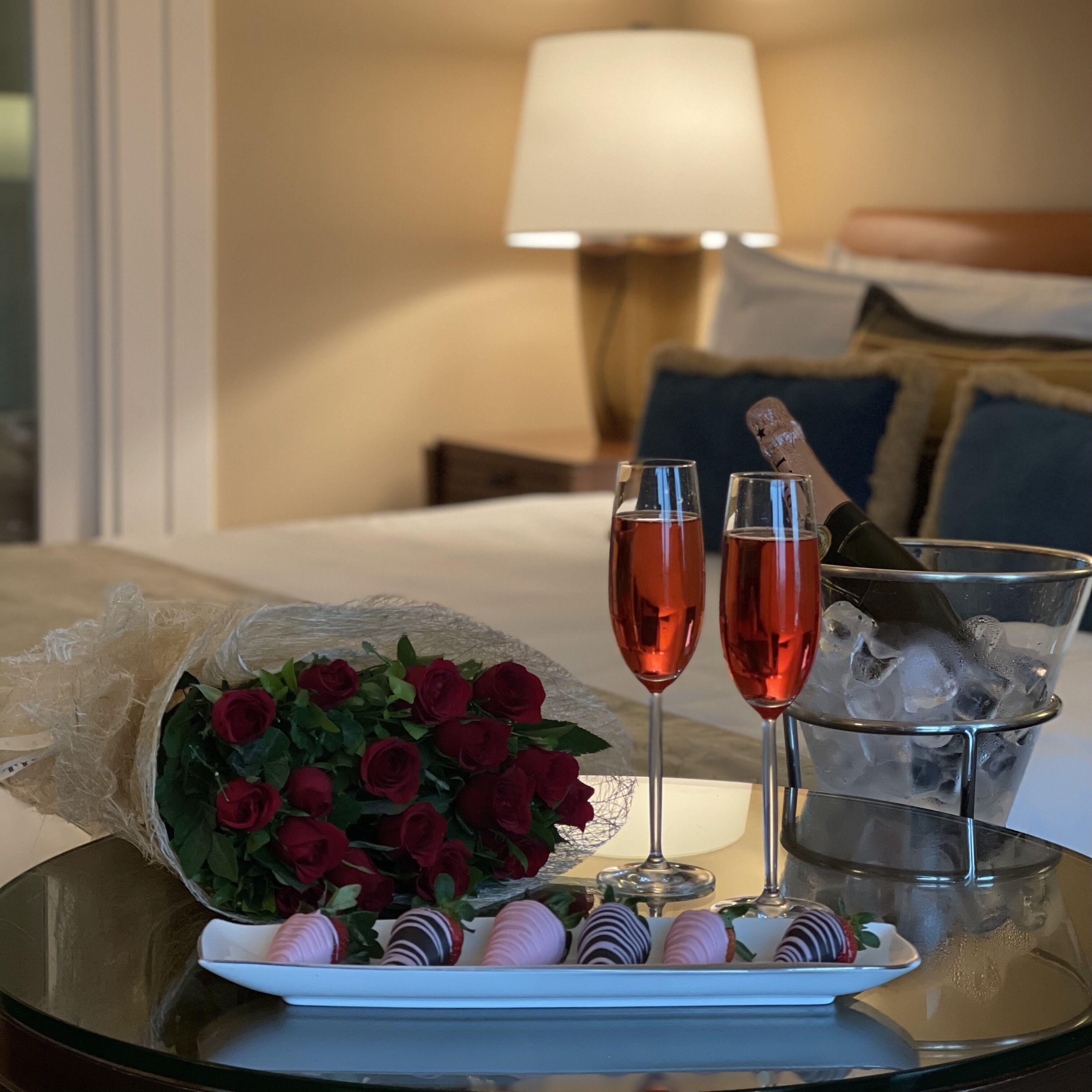 Ein Tisch mit einem Rosenstrauß, zwei Sektgläsern mit Eiswürfeln und Schokoladen-Erdbeeren.