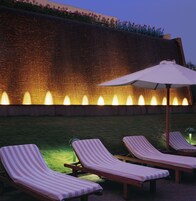 Un área de descanso al aire libre de noche con cuatro sillones a rayas y una sombrilla grande, iluminada por luces empotradas.
