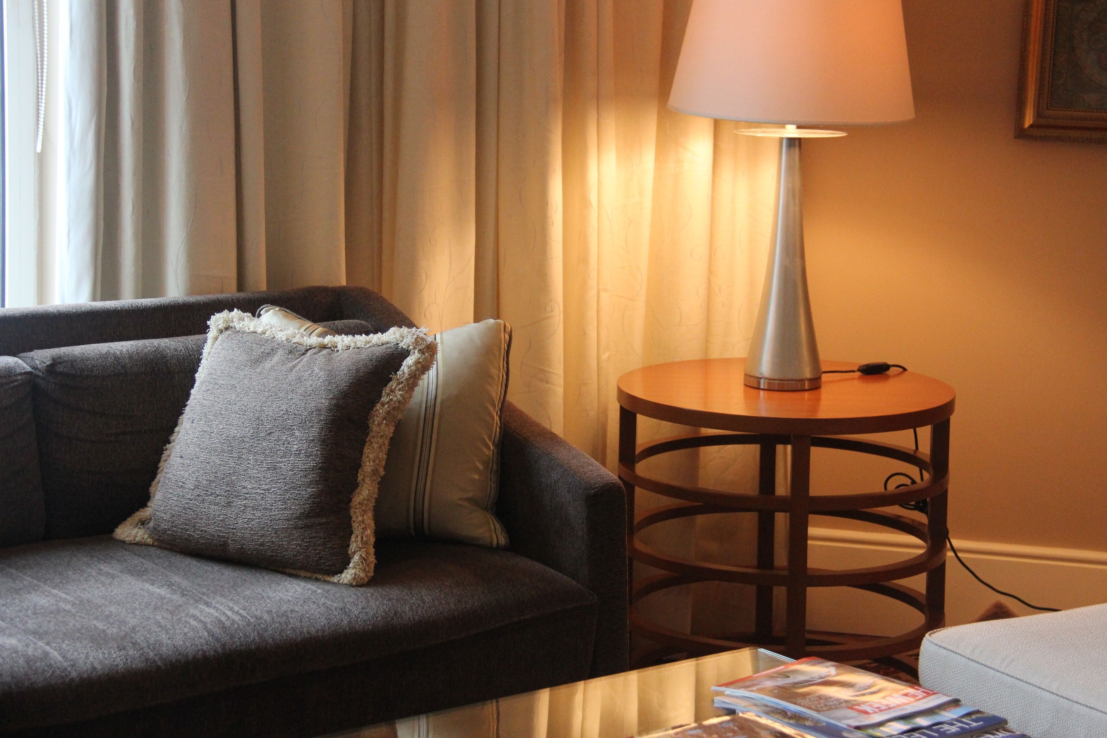 A living room with a sofa, a lamp, and a table with magazines.