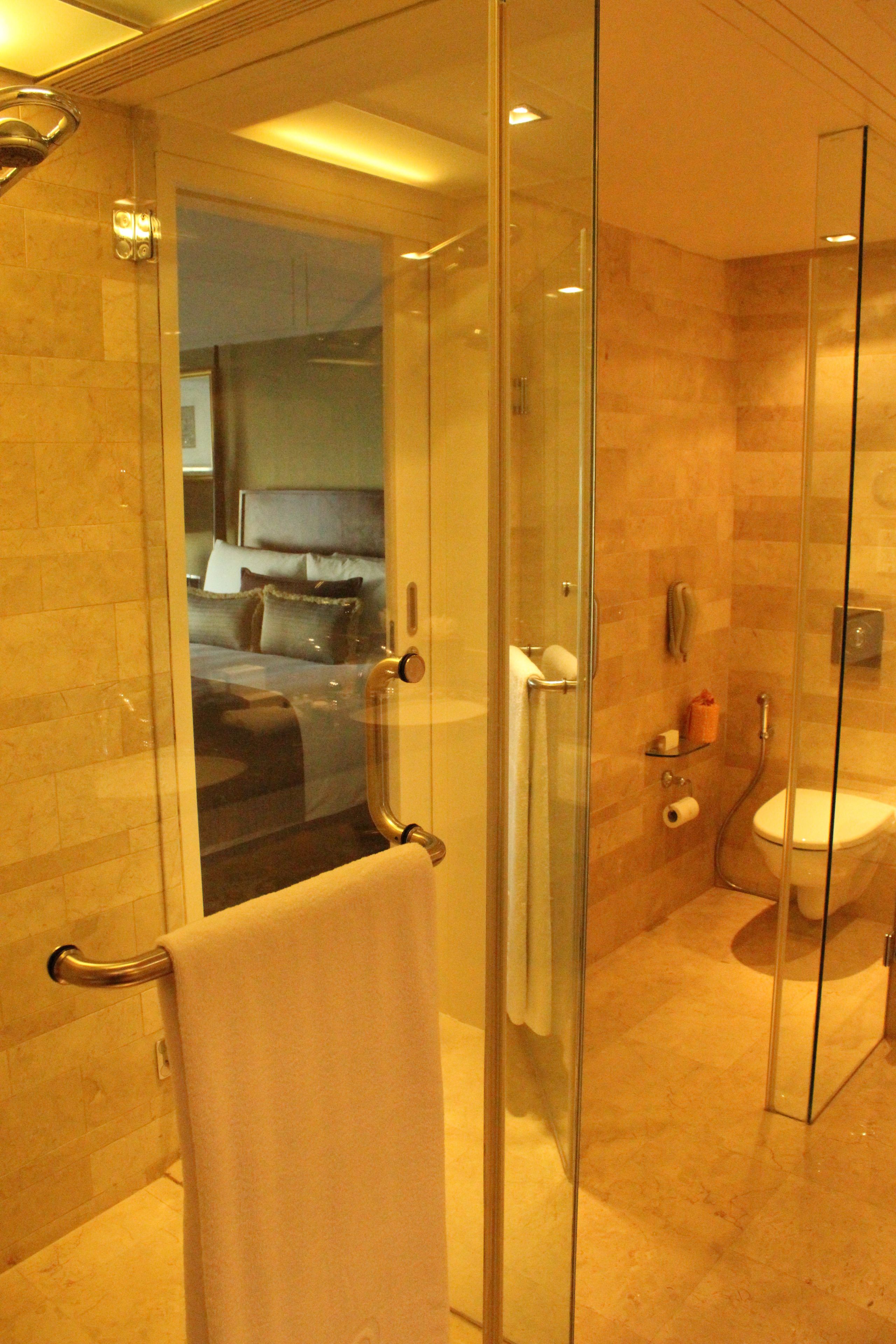 A glass-enclosed shower area with a towel rack, a toilet, and a glass door leading to a bedroom.