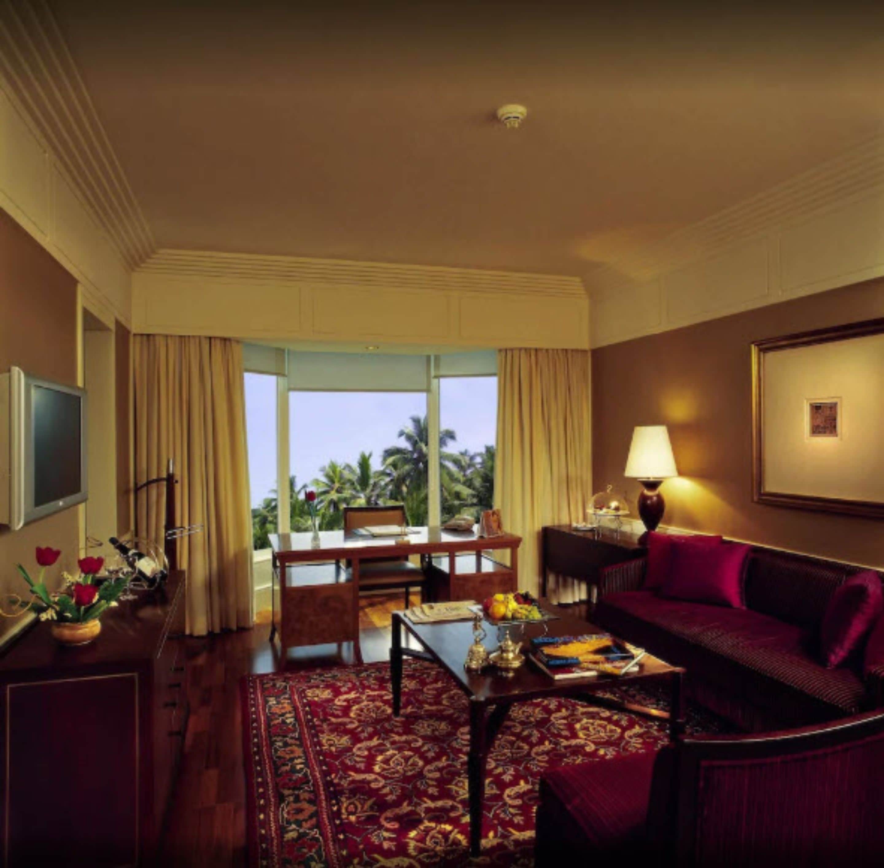 A hotel room with a large window, a dining area, a sofa, a TV, and a lamp.