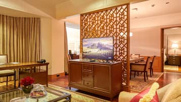 Habitación de hotel con un mueble de entretenimiento de madera, una zona de comedor y un sofá con un cojín decorativo.