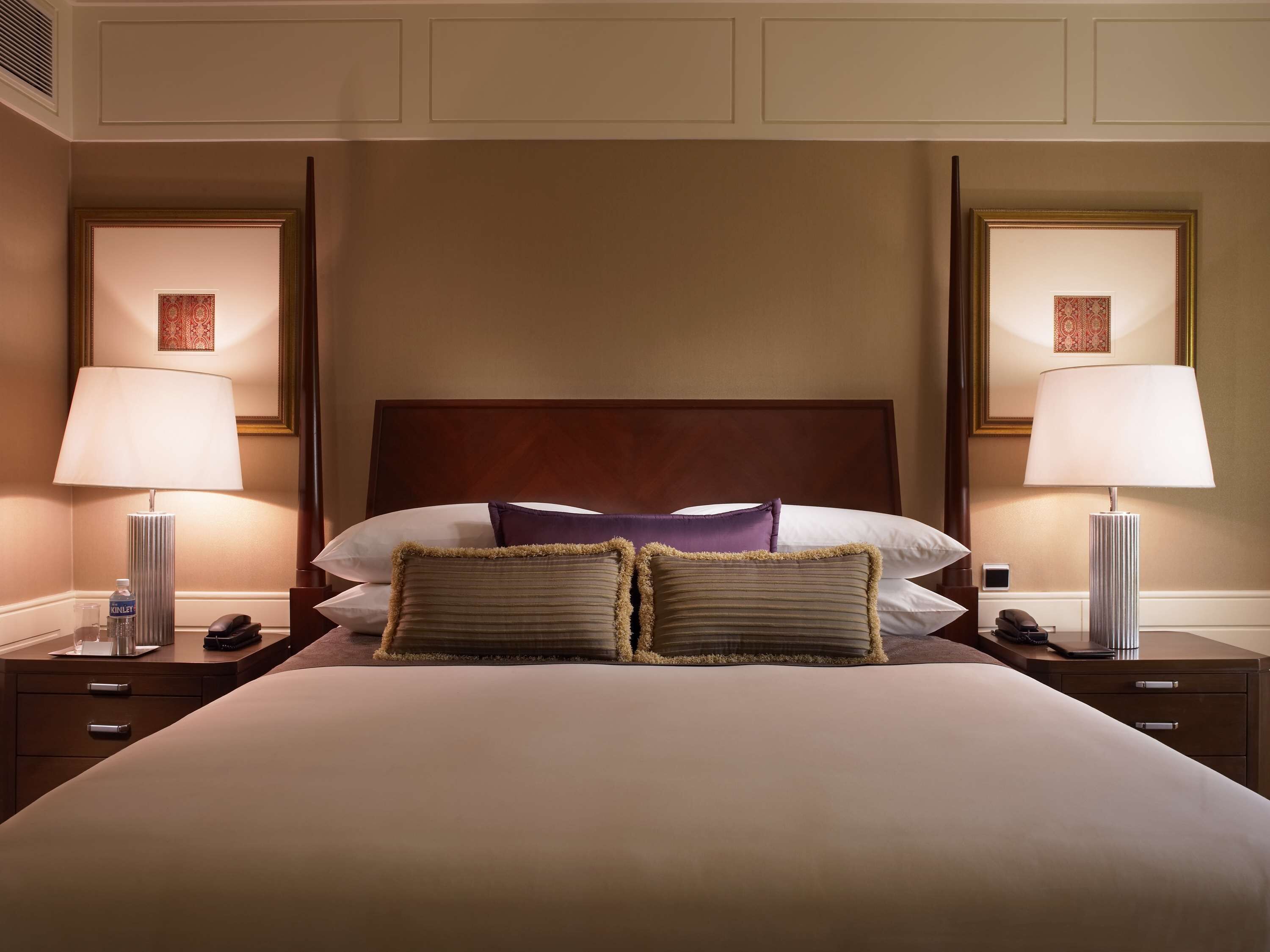 Une chambre d’hôtel avec un grand lit, deux lampes de chevet, une tête de lit en bois et une œuvre d’art encadrée au-dessus du lit.