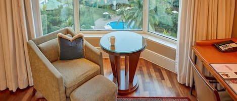 Habitación con sofá, una pequeña mesa y vistas a una piscina y follaje a través de amplios ventanales.