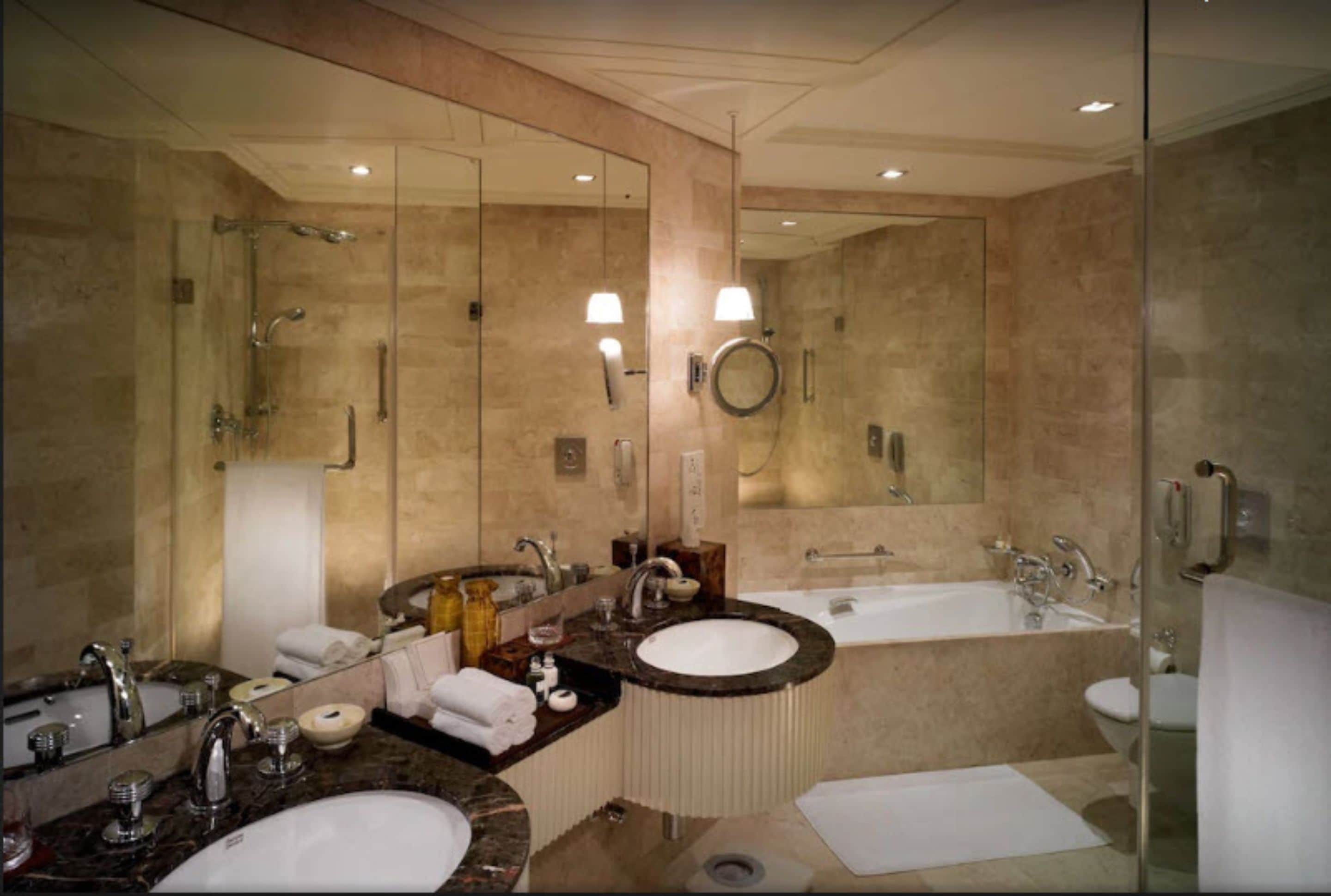 A modern bathroom with two sinks, a large mirror, a bathtub, and a glass shower enclosure.