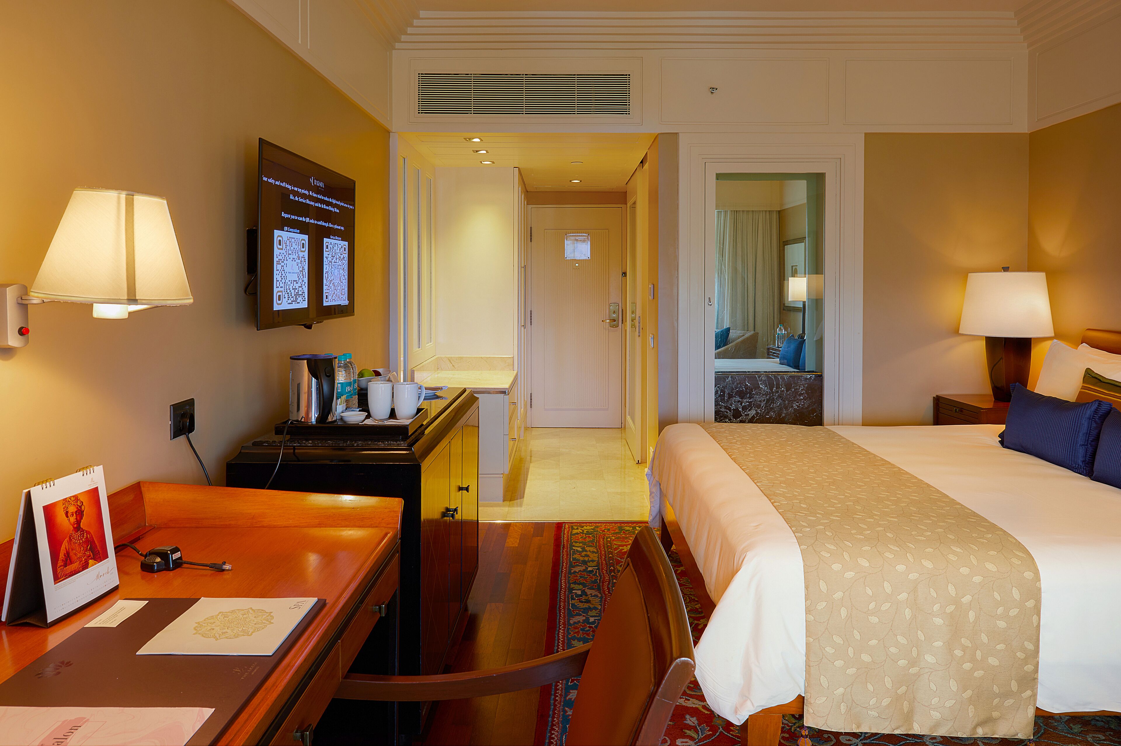 Habitación de hotel con cama, escritorio, silla y televisor mostrando información.
