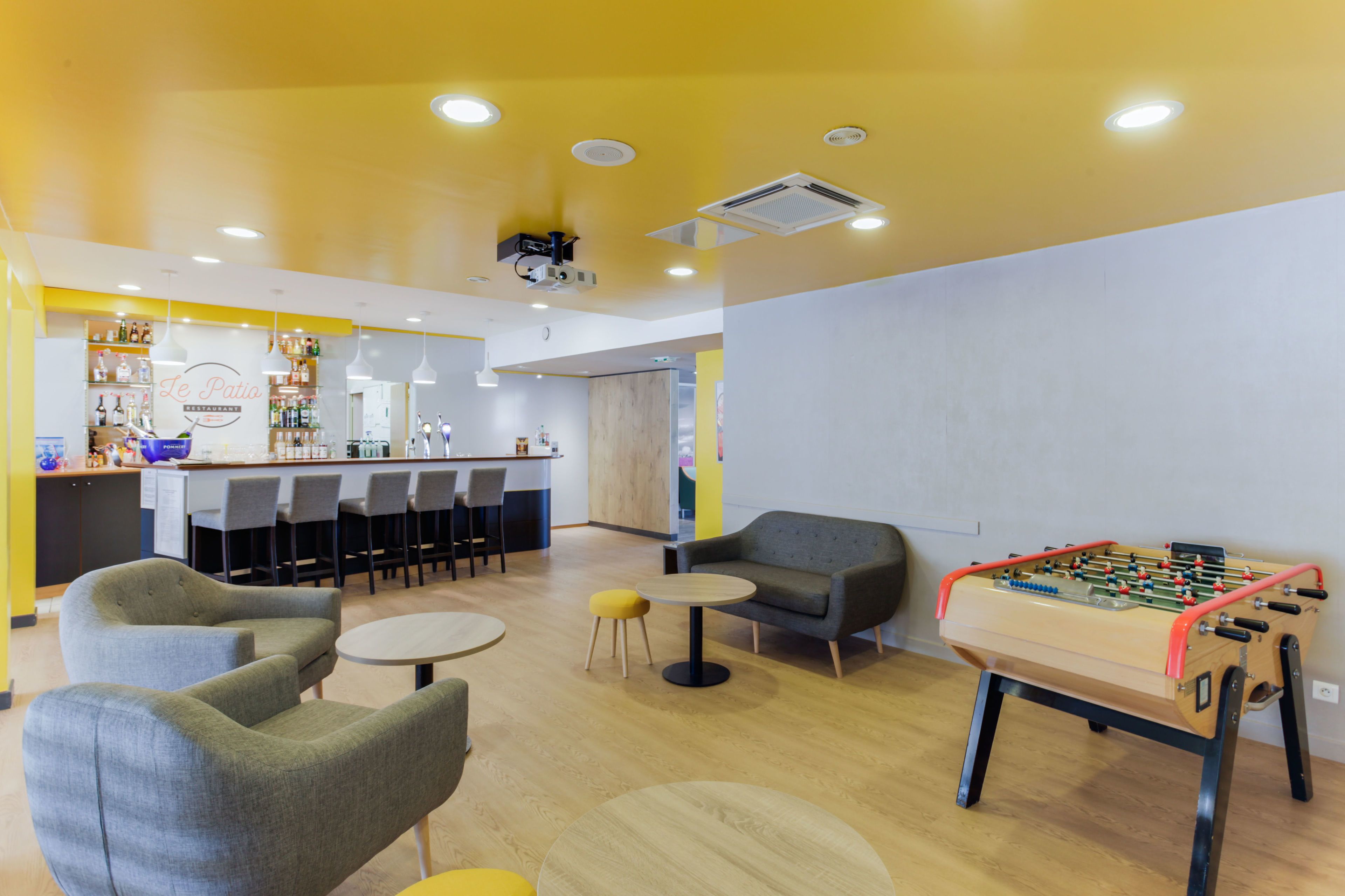 A modern indoor space with seating areas, a foosball table, and a bar area with shelves of bottles.