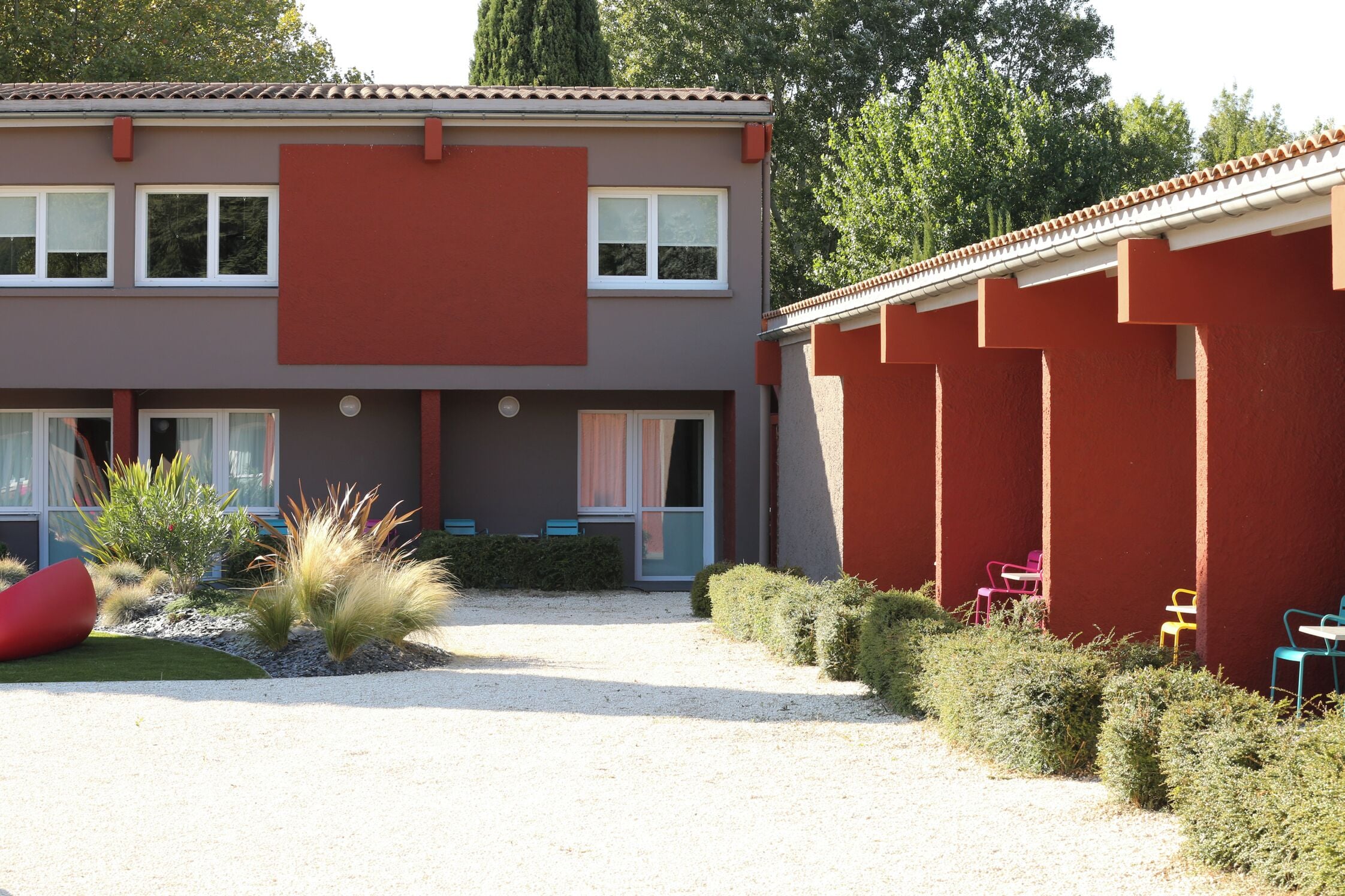 A modern building with a flat roof, large windows, and a gravel driveway.