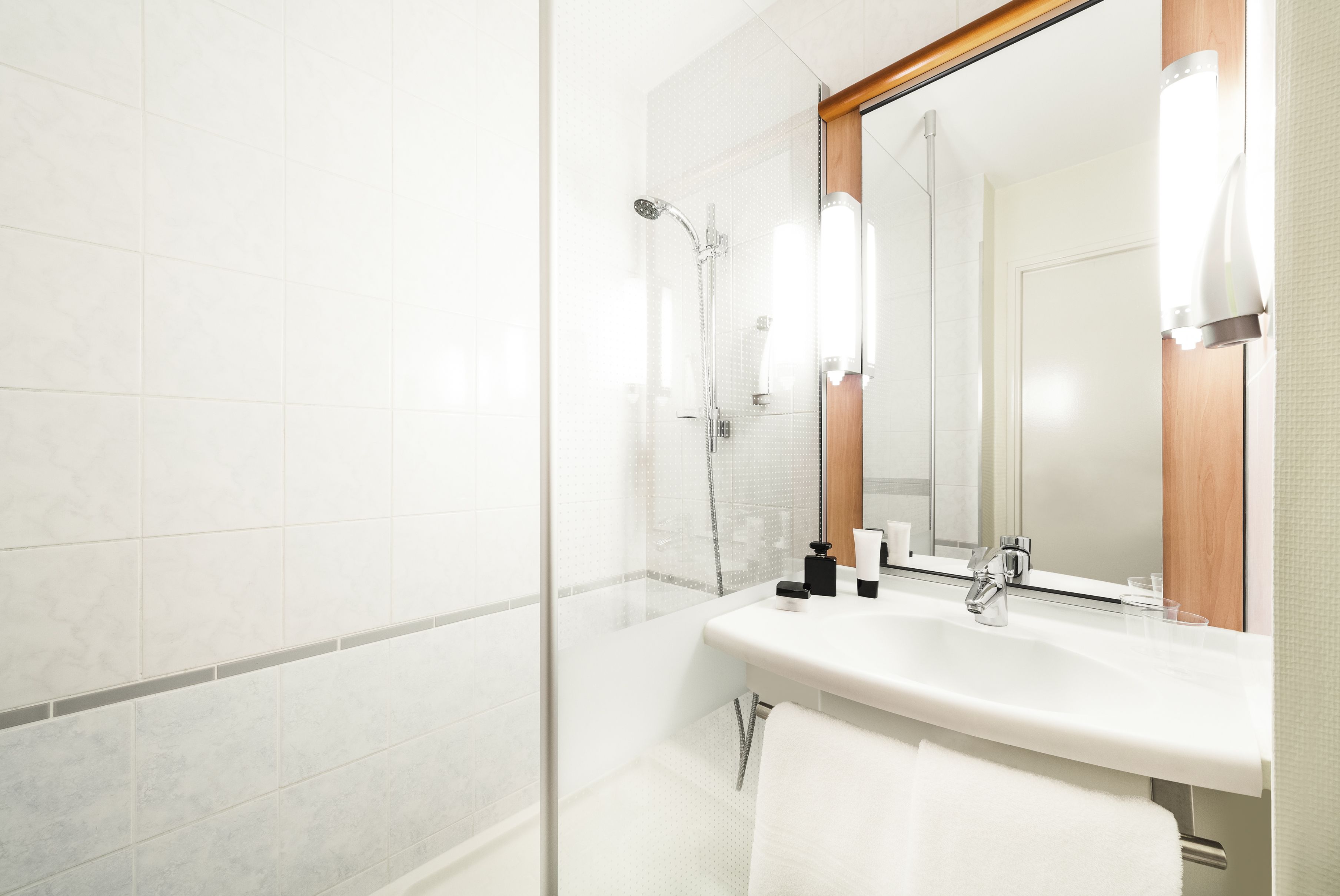 Un baño moderno con cabina de ducha de vidrio, un lavabo blanco y un espejo con marco de madera.