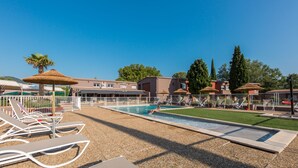 A pool area with lounge chairs and umbrellas, surrounded by buildings and trees. - ibis Montelimar Nord (Saulce-sur-Rhone)