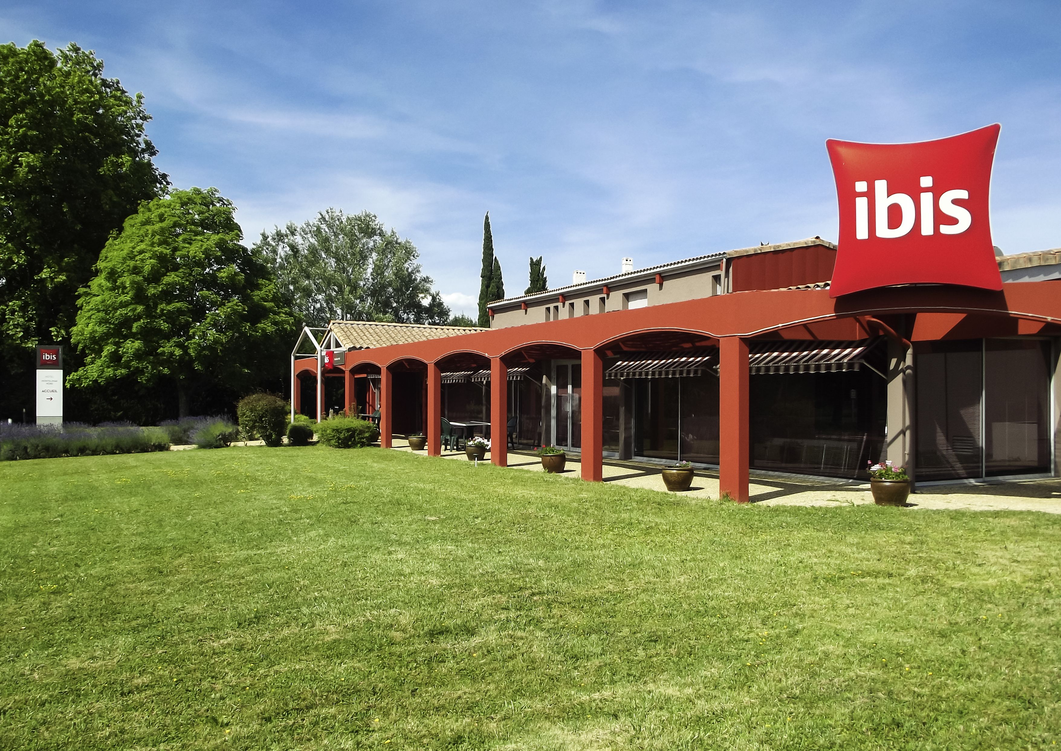 A modern hotel with a red facade, outdoor seating area, and a large 'ibis' sign.