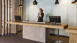 A reception desk with two monitors, a wooden counter, and a modern pendant light. - ibis Montelimar Nord (Saulce-sur-Rhone)