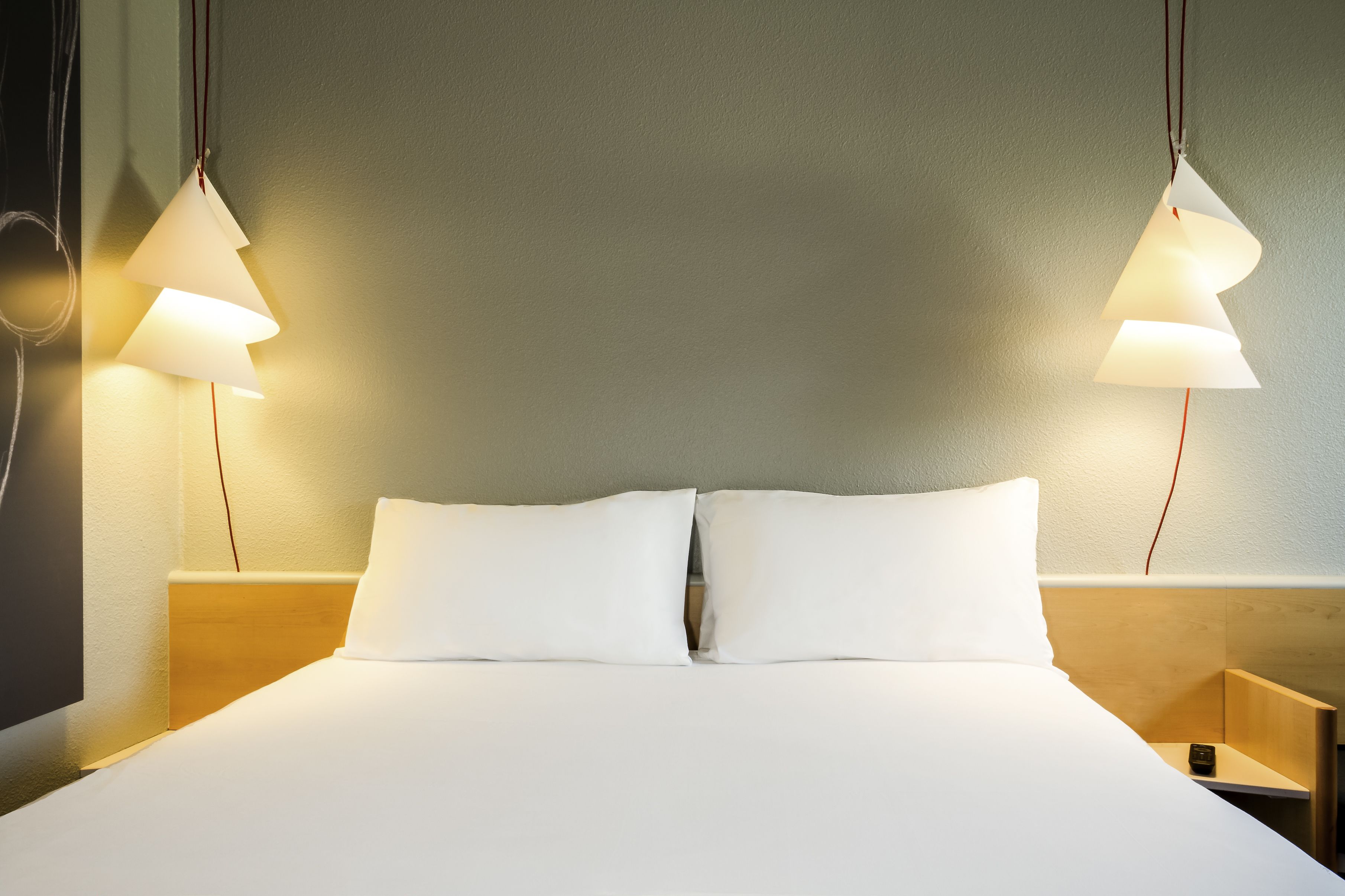 A neatly made bed with white linens and two bedside lamps.