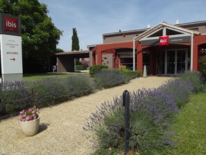 L’entrée d’un hôtel, avec une enseigne indiquant « Montelimar Nord », un chemin de gravier et des plants de lavande.