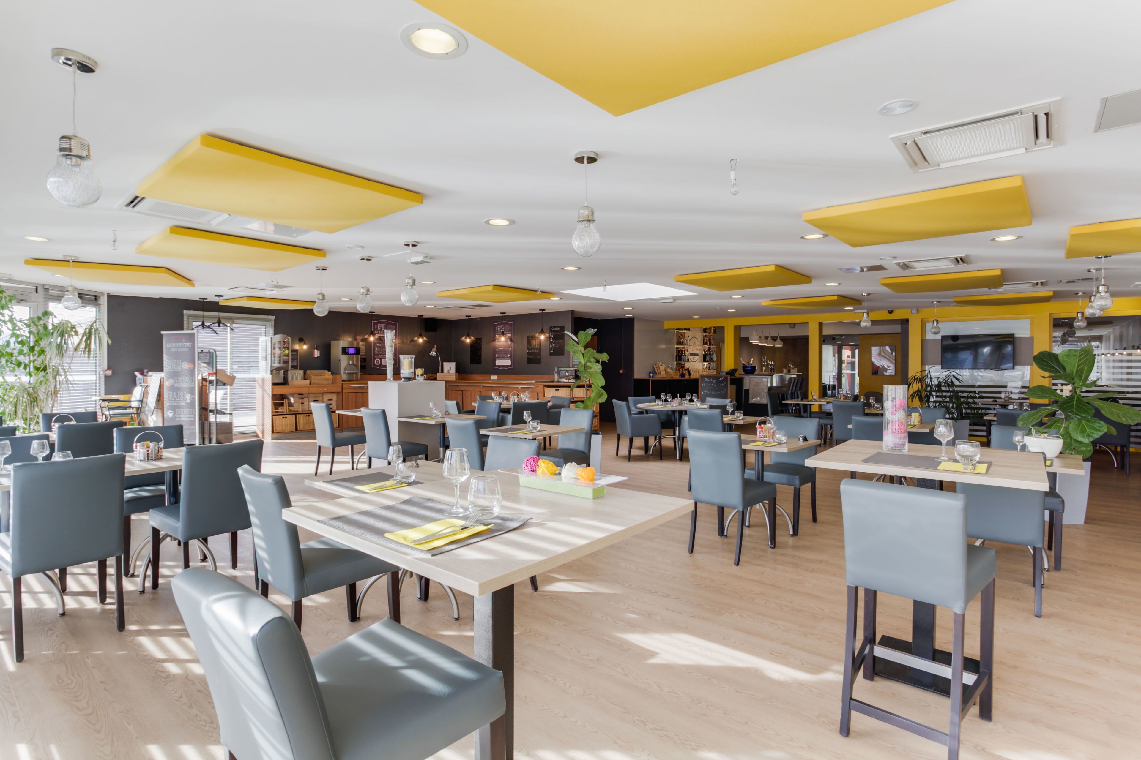 Un restaurante moderno con detalles en amarillo, varias zonas de comedor y una cocina visible al fondo.