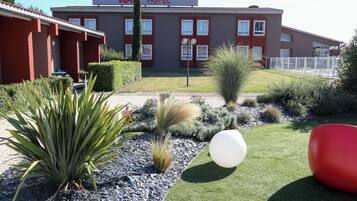 A hotel with a red facade, a signboard, and a well-maintained garden with various plants and a white spherical object.