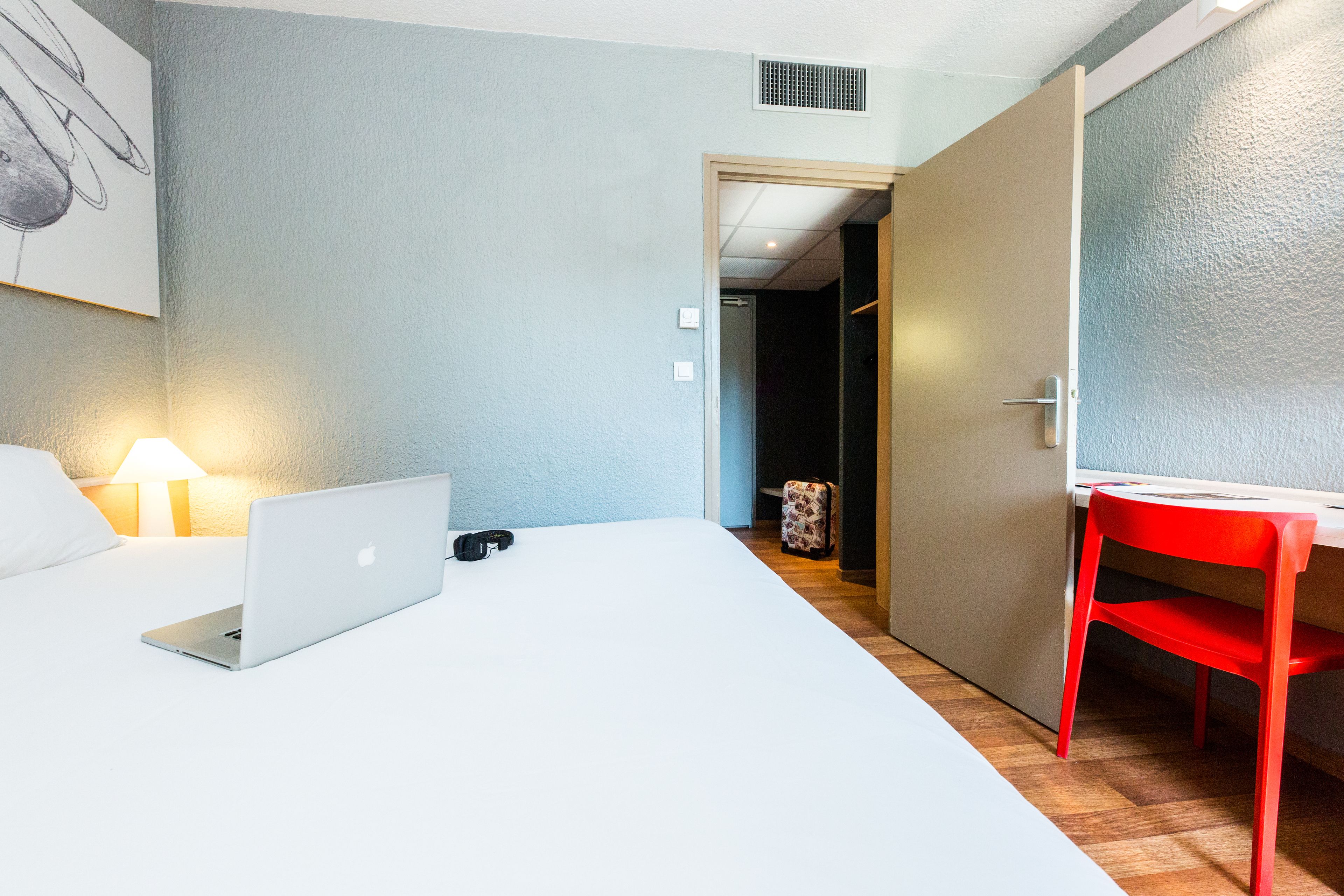 A hotel room with a bed, a desk, a chair, and a lamp.