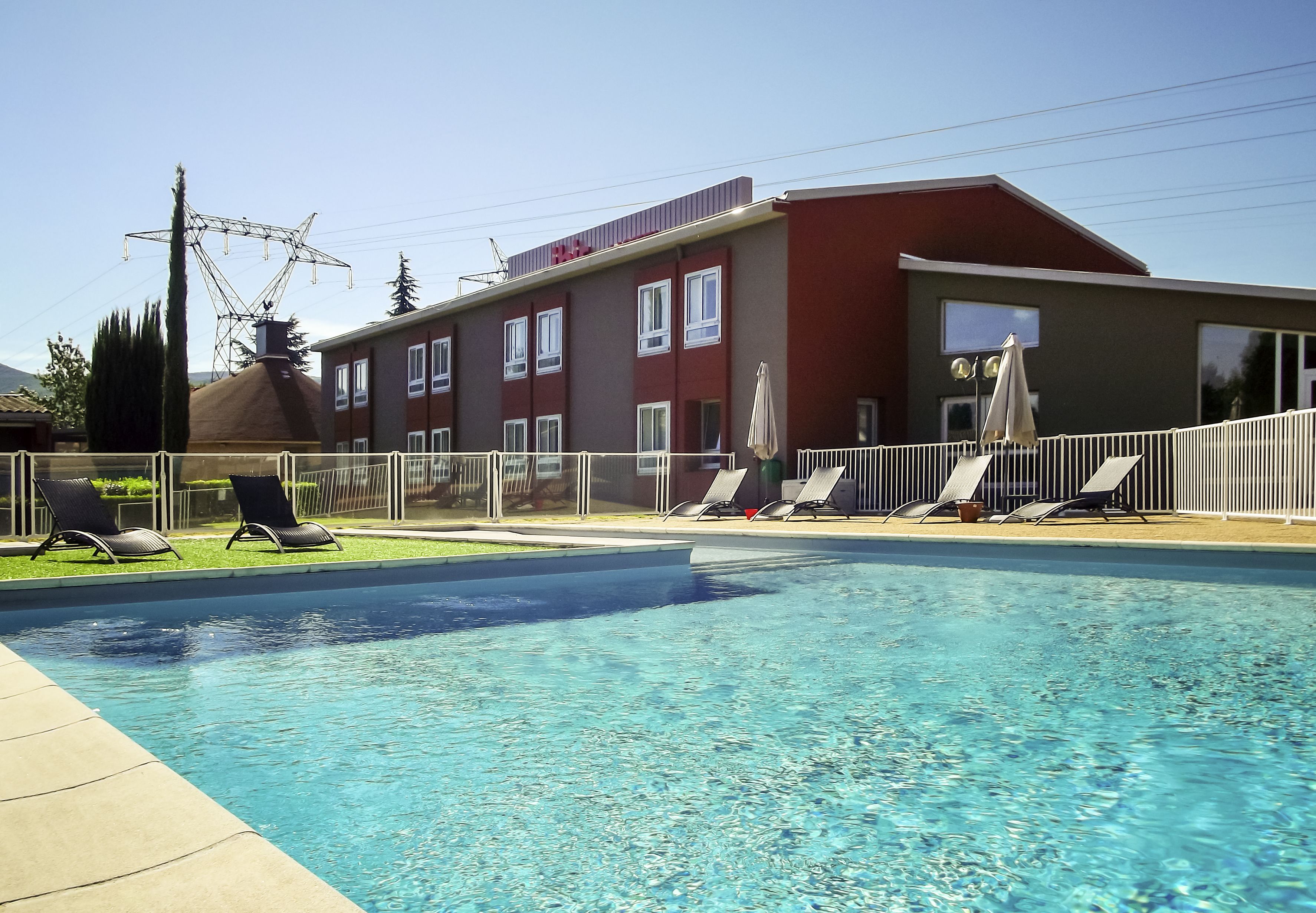 A swimming pool with lounge chairs and a building with multiple windows and a red roof.