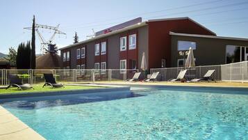 A swimming pool with lounge chairs and a building with multiple windows and a red roof.