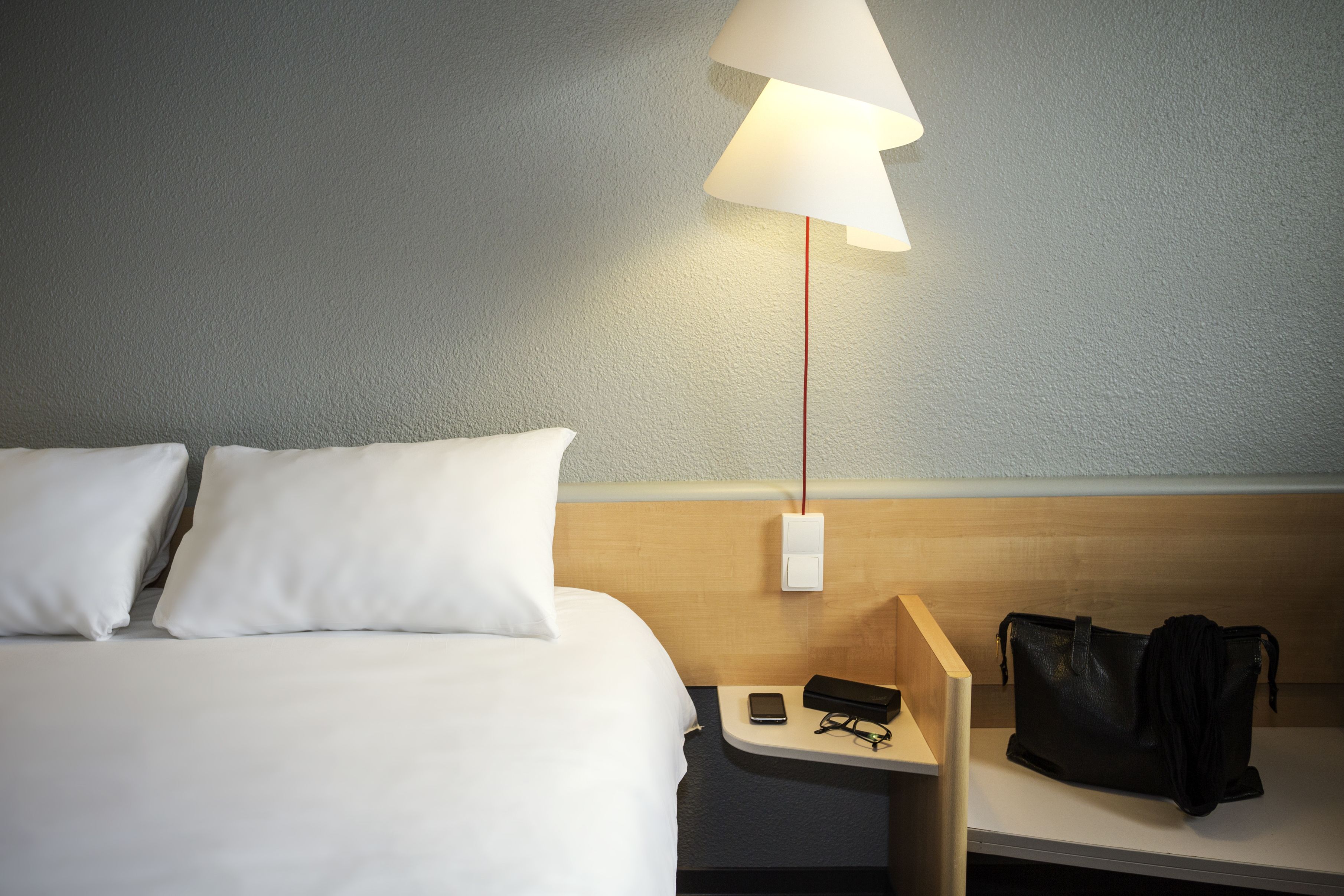 A hotel room with a bed, a nightstand, a lamp, and a black bag.