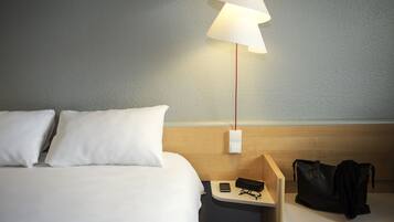 A hotel room with a bed, a nightstand, a lamp, and a black bag.