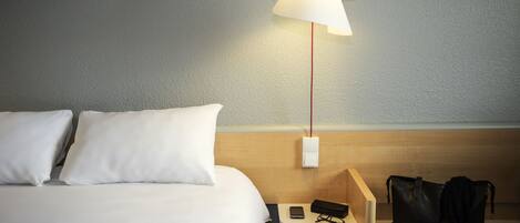 A hotel room with a bed, a nightstand, a lamp, and a black bag.