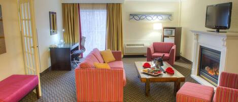 Habitación de hotel con sofá, sillones, mesa de centro, televisión y chimenea.