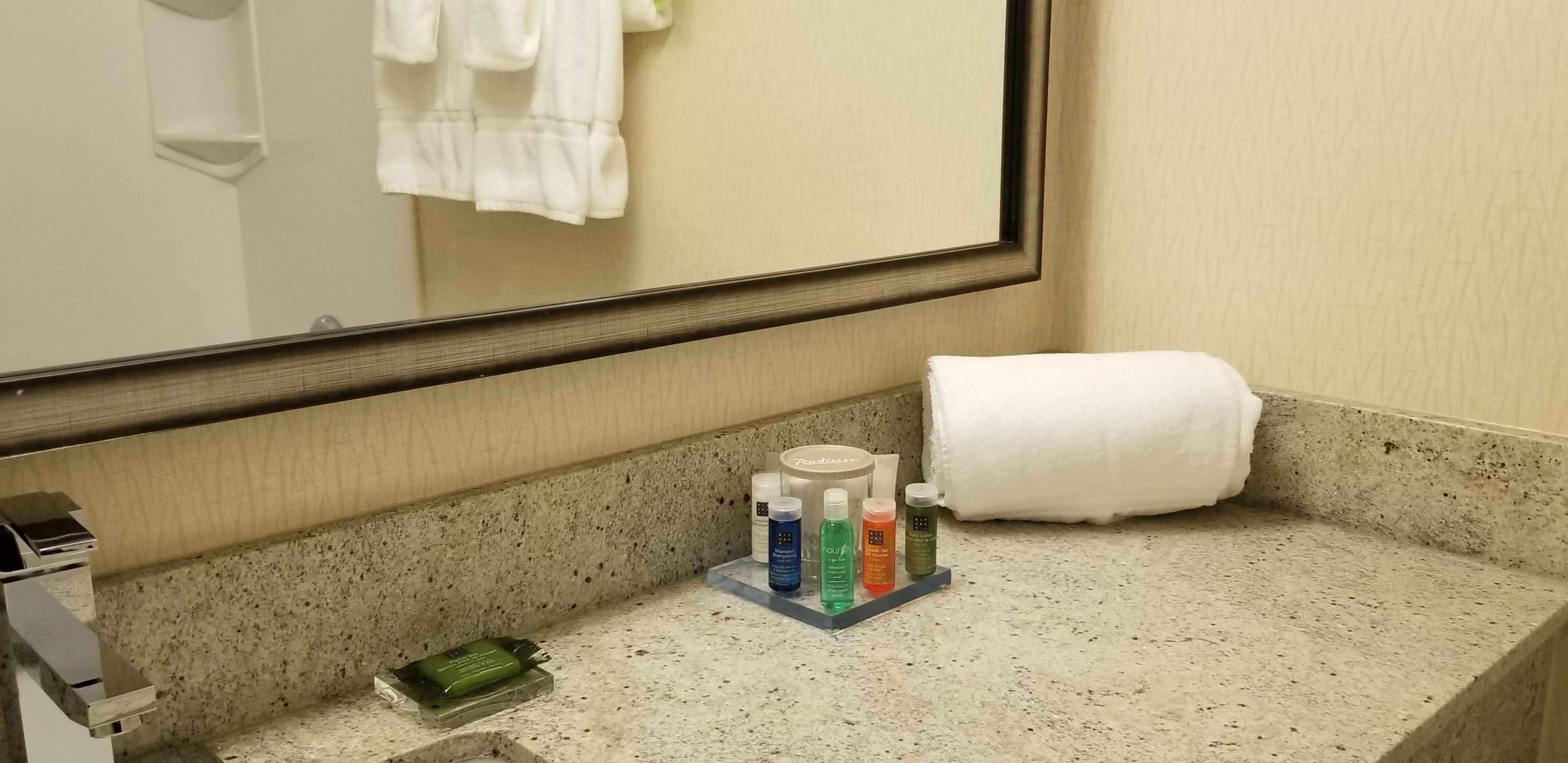 Un bagno con un piano di lavoro in granito, uno specchio, un asciugamano e articoli da toilette.