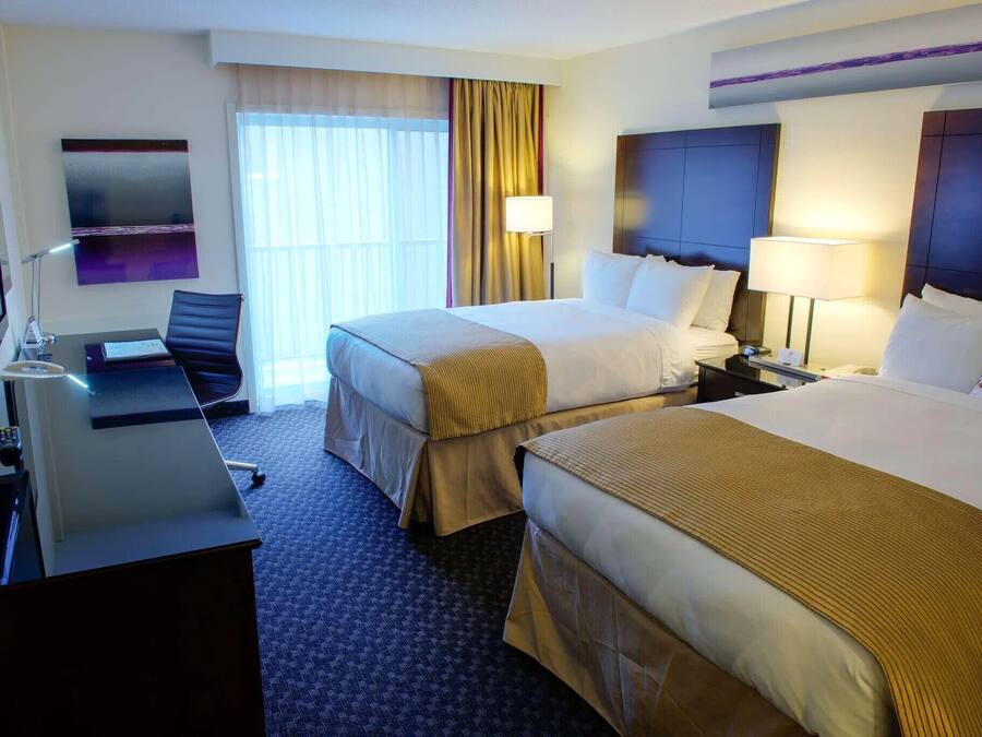A hotel room with two beds, a desk, a chair, a TV, and a window with curtains.