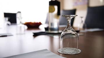 Un decantador de vidrio transparente sobre una mesa con un posavasos de encaje, un cuaderno y un fondo desenfocado con una lámpara y un jarrón.